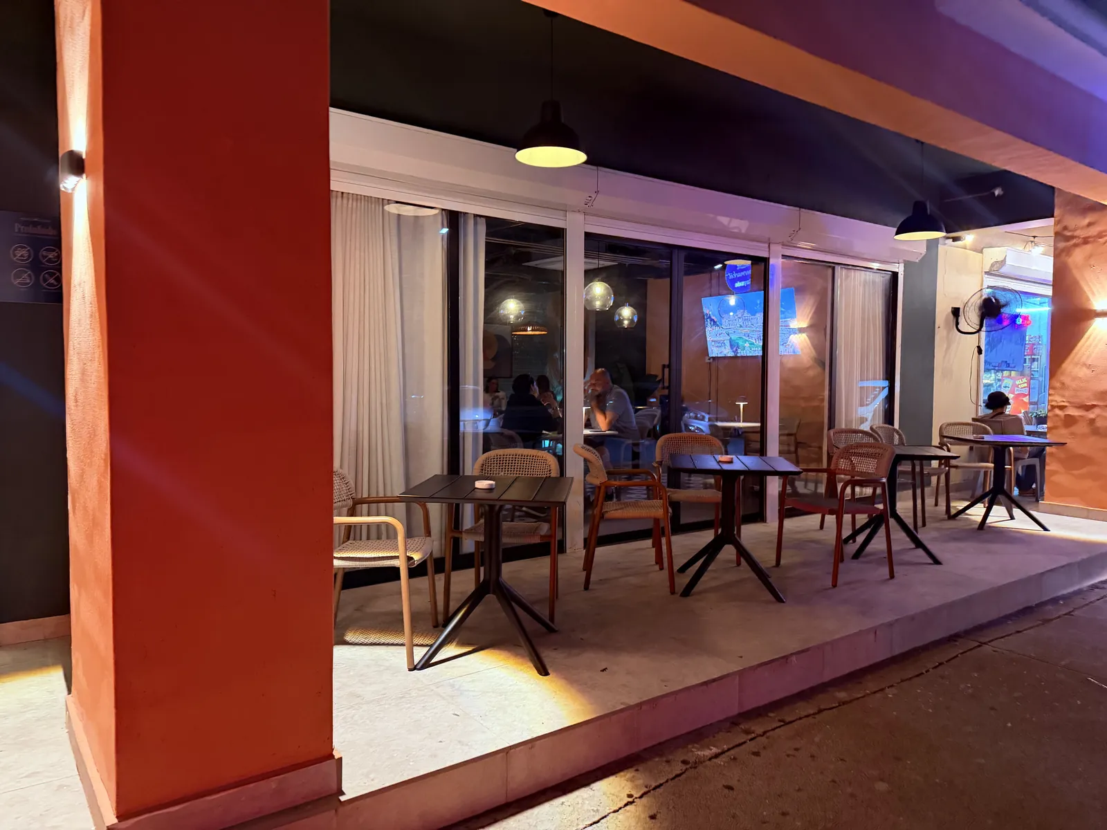 The covered terrace at night, tables and chairs under the arcade